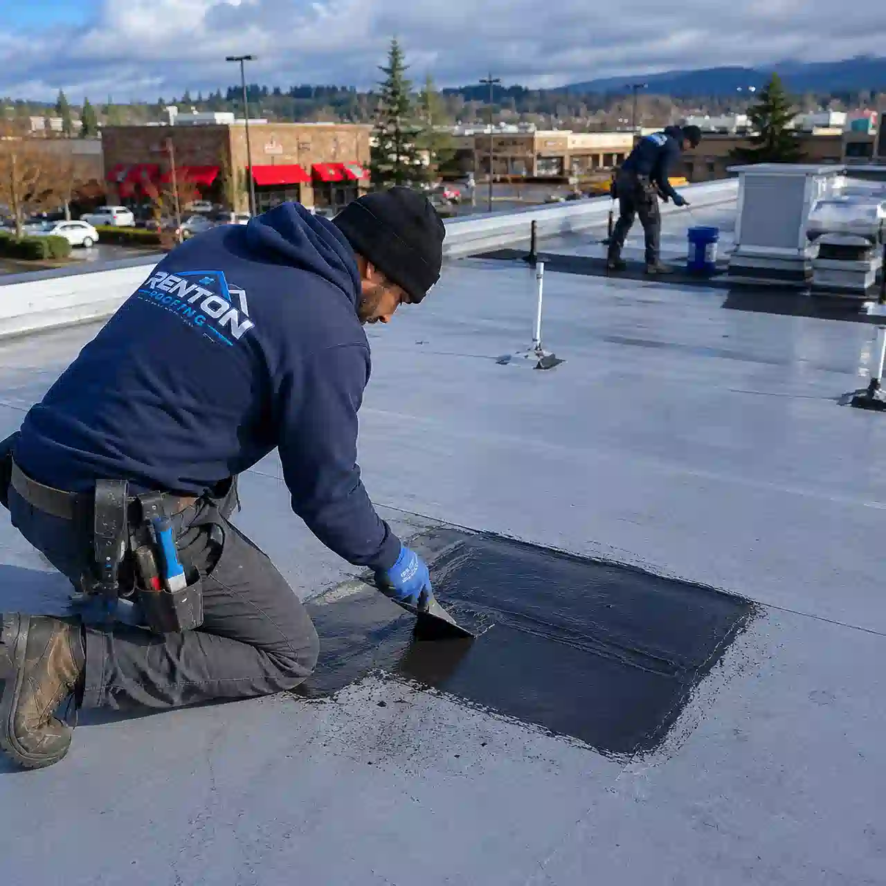 Renton Roofing technician clearing a roof drain at a retail strip mall